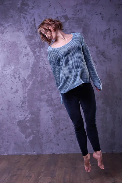 Güzel genç kız stüdyoda atlama poz bir gri örgü kazak ve siyah kadife tozluk, yalınayak, kahverengi kıvırcık saçlı. Moda fotoğraf kadın dansçı modeli Studio gri arka plan ile