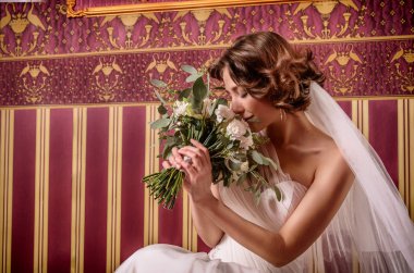 Güzel gelin ile muhteşem bir çok beyaz dantel gelinlik peonies, gül romantik bir buket, lüks bordo iç, moda fotoğraf portre içinde oturan bukleler akan.