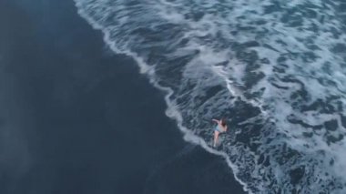 Siyah kum ve güzel mutlu genç erkek kot şort ve sahilde, video 4 k uçak yukarıdan çekim harika görünümü poz gri tişört ile Bali günbatımı, dalgalar okyanus plaj havadan görüntüleri