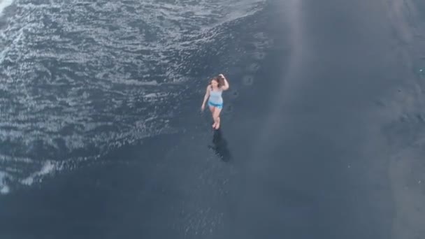 海洋海滩与黑色的沙子和波浪在巴厘岛的空中视频与美丽的快乐年轻的步行女性模特牛仔裤短裤和灰色 拍摄视频4K 从上面的飞机 美妙的景色 — 图库视频影像