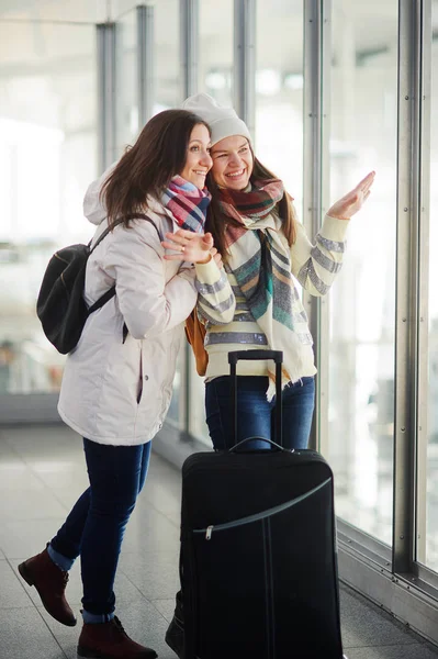 Två unga kvinnor tittar genom fönstret på flygplan på flygplatsen. Stockbild