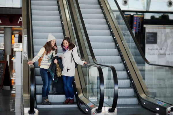 Dos chicas bajan por la escalera mecánica en el aeropuerto . Imágenes de stock libres de derechos