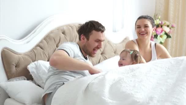 Dos padres con una niña en la cama jugando y riendo felizmente — Vídeo de stock