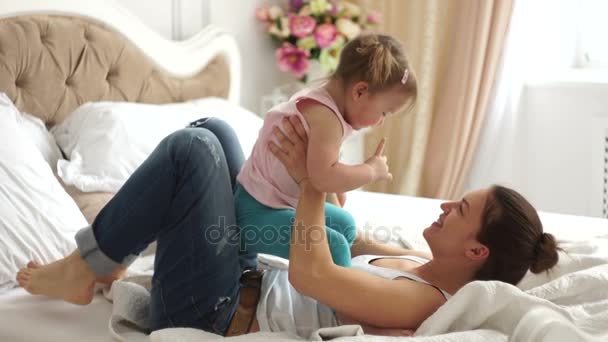 Молодая мать и маленькая девочка играют, лежа в постели — стоковое видео