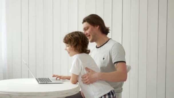 Un jeune homme occupé travaille à la maison sur un ordinateur portable et prend également soin de son fils . — Video