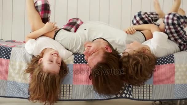 Mladá rodina - otec a jeho děti si hrají na posteli. — Stock video