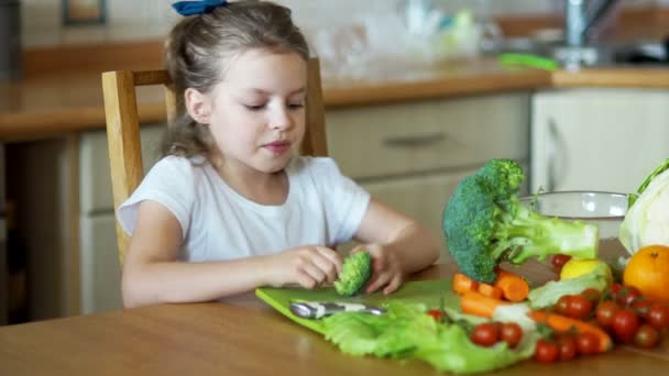 Dívka jíst brokolici sedí u kuchyňského stolu. — Stock video
