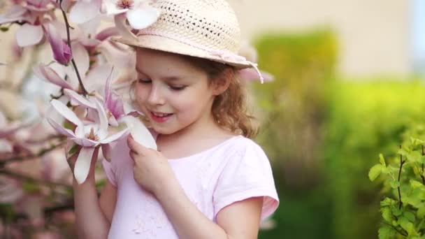 Vacker liten flicka att lukta blommor av Magnolia i trädgården. — Stockvideo