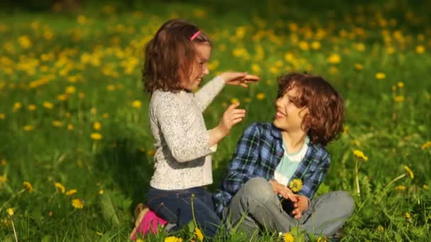 Хлопчик і дівчинка розважаються на весняній траві . — стокове відео