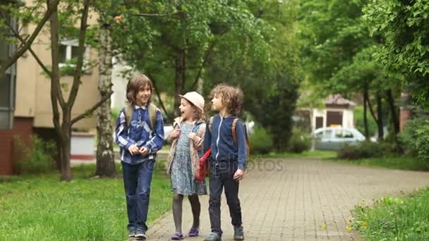 Tres niños van a la escuela. Detrás de ellos, llevan mochilas. Los niños están hablando animadamente. De vuelta a la escuela. Fin de las lecciones — Vídeos de Stock