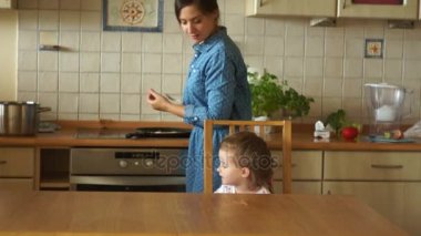 Anne yumurta ocakta pişiriyor. Küçük bir kızın kahvaltı masasında bekliyor. Kız çok kızmış. Çocukça whims. Ailece Kahvaltı.