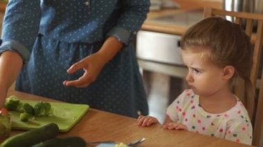 Küçük kız annesi ile mutfakta. Anne kızı brokoli olarak verir. Kız kararlı sebze eliyle iter. Bebek çok kızgın ve yemek istemiyor.