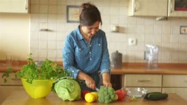 Bir esmer bir kot elbise mutfak masasında dans ediyor. Kız havuç kesiyor. Sağlıklı yaşam tarzı.