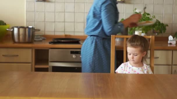 Mother and daughter having healthy breakfast in kitchen. The girl is not hungry. She refuses to eat, pushes the plate aside. Poor appetite. — Stock Video