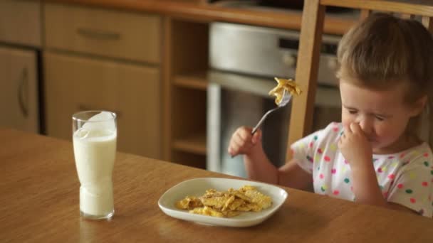 Le bébé mange des œufs dans la cuisine. Il essaie un morceau avec une fourchette et repousse la plaque. Aliments chauds . — Video