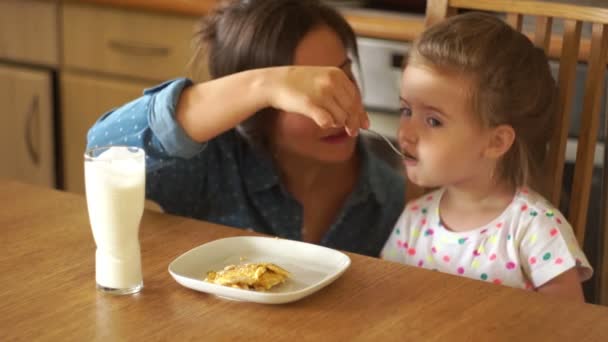 A little girl eats scrambled eggs. Mom feeds her with a fork. Both girls are very happy. — Stock Video