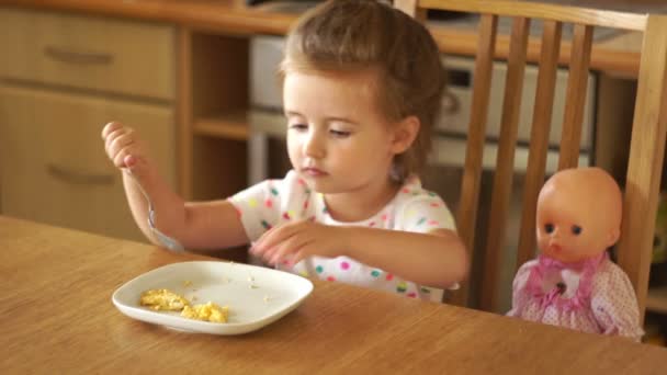 La chica está alimentando a la muñeca en la cocina. Toma la comida con las manos y se la come ella misma. Juego de las madres — Vídeo de stock