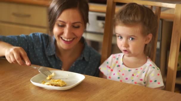 Eine glückliche Mutter füttert eine kleine Tochter. Mama spielt eine fliegende Rakete. öffnet das Mädchen den Mund weit. mütterlicher Kuss, guter Appetit. — Stockvideo