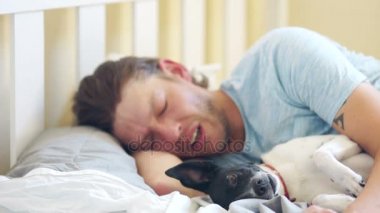 Genç bir yetişkin adam köpeğiyle yatağında uyuyor. Lisans sabah. Köpek sahibi uyanır