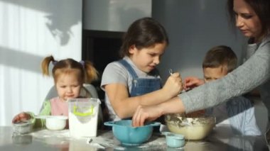 Üç çocuk mutfakta hazırlayın. Büyük kız kardeşi kardeşi genç çalış un ile hamur hitap etmek için yardımcı olur. Anne Çocuk burun un ile bir şaka olarak kirli. Tuhaf ailenin