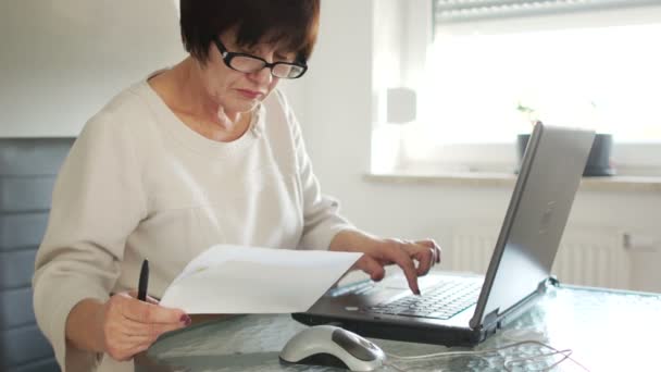 Een zakenvrouw betaalt rekeningen met behulp van een computer, betalingen via internet, internetbankieren. In haar hand heeft ze een pen en papier — Stockvideo