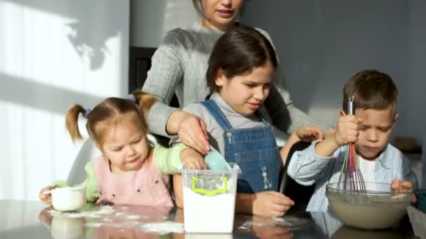 Mama i dzieci w kuchni. Troje dzieci wyrabia ciasto i grać z mąki. Żart, zabawa, nauczyć się gotować grając — Wideo stockowe