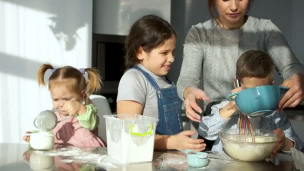 Una familia alegre de dos adultos y tres niños amasa la masa en la cocina. Mamá y papá ayudan a los niños y ríen felices. Todos estaban sucios en harina. — Vídeos de Stock