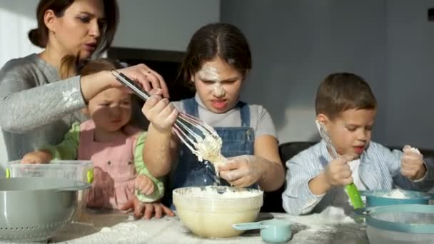 Прекрасная мать с тремя весёлыми детьми разного возраста разминает тесто. Старшая дочь снимает тесто с короллы. — стоковое видео