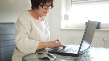Yaşlı bir kadın ile bir dizüstü bilgisayar ve bir banka kartı faturaları ödüyor. Online ödemeler. Hipermetrop
