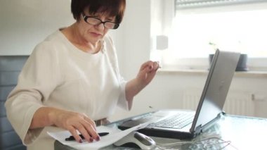 İş kıyafeti ve gözlük bir kadın onu laptop ile çalışıyor. Kağıt hesapları yakın vardır. Rakamlar, miyopluk göz önünde eğilir