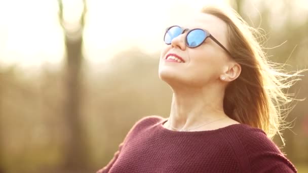 Eine schöne dreißigjährige Frau mit Brille legt ihr Gesicht in die Frühlingssonne. er reiht seine Hände auf und geht dem Wind entgegen. Einheit mit der Natur. Die Frühlingshitze genießen — Stockvideo