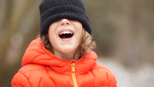 Retrato de um menino em um gorro de malha de inverno. Seus olhos estão fechados com um chapéu, ele ri — Vídeo de Stock