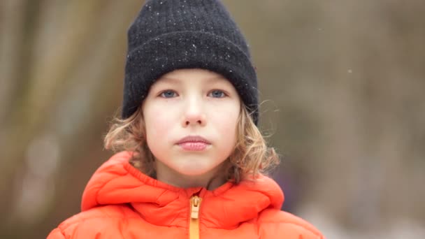 Retrato fechado de um menino europeu em um chapéu de inverno. Ele é sério, chateado, e depois começa a sorrir — Vídeo de Stock