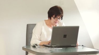 Orta yaşlı bir kadın concentratedly bilgisayarda çalışıyor. O iş hakkında tutkulu ve kendi kendine konuşuyor.