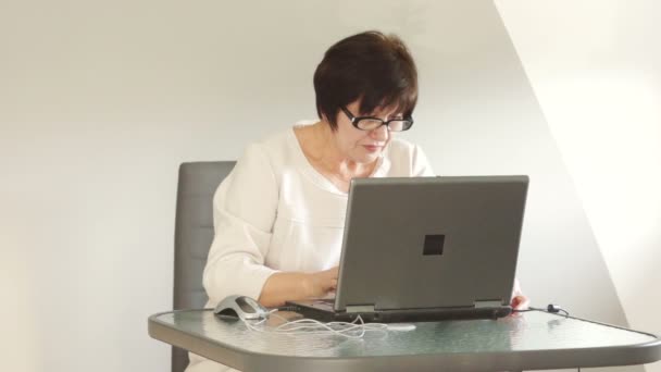 Femme âgée avec un ordinateur portable à l'intérieur salle de lumière . — Video