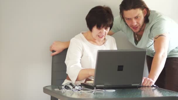 Deux employés de bureau travaillent à l'ordinateur. Un jeune homme aide un collègue âgé. Administrateur réseau — Video