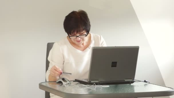 Een middelbare leeftijd vrouw maakt een betaling in een online winkel. Internet winkelen, online diensten voor gepensioneerden — Stockvideo