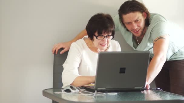 Молодой сотрудник помогает пожилому коллеге справиться с новой компьютерной программой. Стреляет жестом вверх большим пальцем, все в порядке — стоковое видео