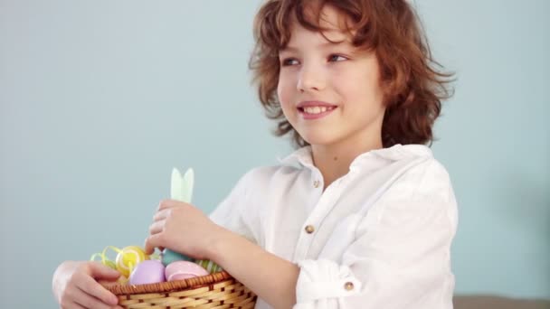 Cheerful schoolboy with a basket of Easter eggs. Curly-haired boy laughs fun — Stock Video