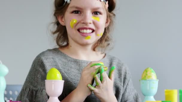 Cute little girl painting colorful easter eggs. She dirty her hands and face — Stock Video