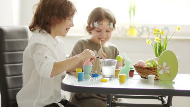 Broer en zus verf paaseieren thuis in de keuken. Ze zijn zich te concentreren. Penselen en verf, childrens creativiteit — Stockvideo