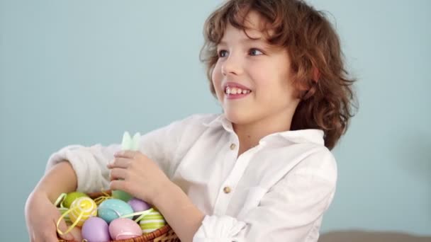 Studioporträt eines fröhlichen Jungen mit einem Osterkorb in der Hand. rothaariges, lockiges blauäugiges Kind — Stockvideo
