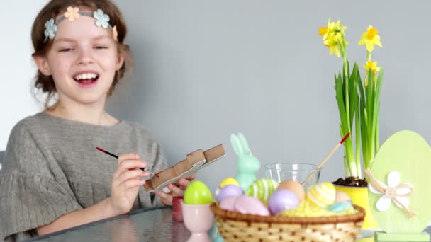 Easter decor. The girl paints the figure of the Easter bunny. The child looks at the frame and laughs. Child creativity, development of artistic abilities — Stock Video