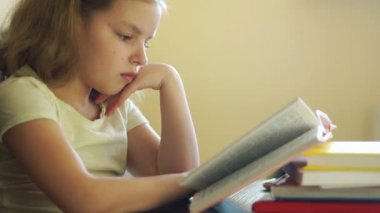 Bir kız öğrenci bir masada otururken kitap okur. Evde eğitim. Çocukların eğitimi. Bilgi günü