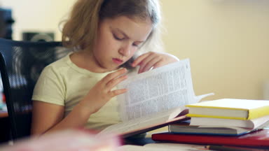 Bir kız öğrenci bir masada otururken kitap okur. Evde eğitim. Çocukların eğitimi. Bilgi günü