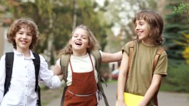 Üç okul, çocuklar ve kız okula gidiyor. Omuzlarının okul arka çantalar vardır. Kız çocuklar neşeyle sarılma. okul dostluk. Okula dönüş