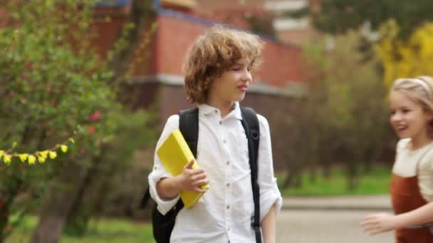 Menina e menino, as crianças em idade escolar abraçam alegremente. Amizade escolar, primeiro amor. Curly, crianças elegantes. De volta à escola. Casal de adolescentes — Vídeo de Stock