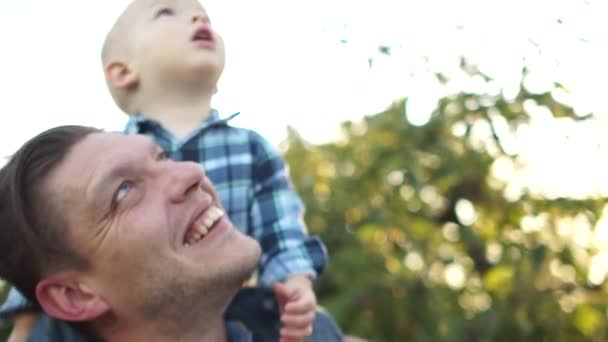 Ojciec i syn cieszą się świeżym powietrzem. Dzieciak siedzi na ramionach swoich ojców, oboje patrzą w niebo, dzień ojców. — Wideo stockowe
