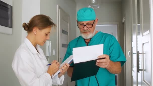 Pielęgniarka w białym płaszczu podpisuje papiery z dyrektorem kliniki. Personel medyczny w pracy — Wideo stockowe