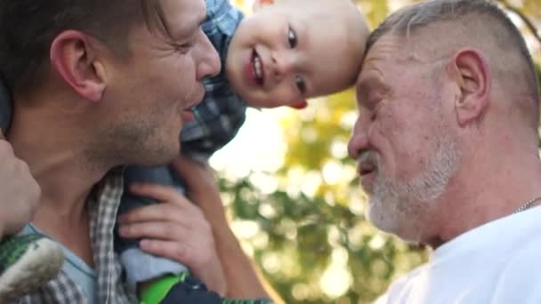 Счастливый молодой человек со своим маленьким сыном и пожилым отцом. Три поколения мужчин одной семьи, близкий портрет в летнем саду, день отца — стоковое видео